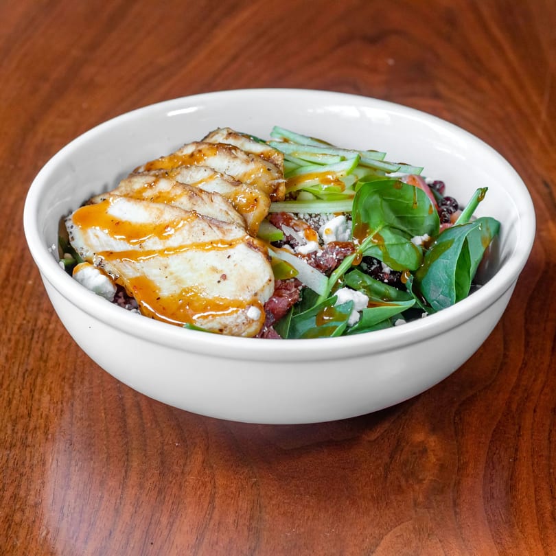 Grilled chicken slices with orange sauce, spinach, and feta cheese in a white bowl on a wooden table.