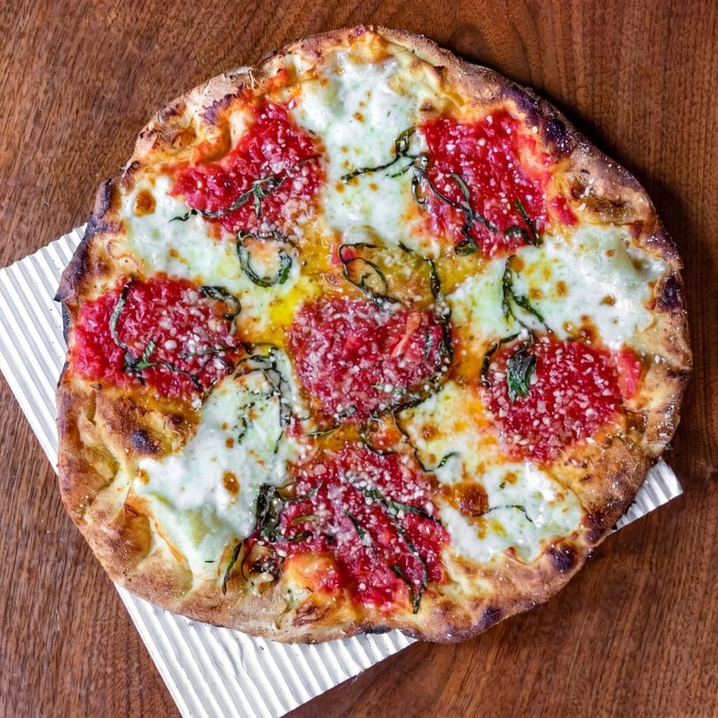 A whole margherita pizza with fresh basil, mozzarella, and tomato sauce on a wooden table.