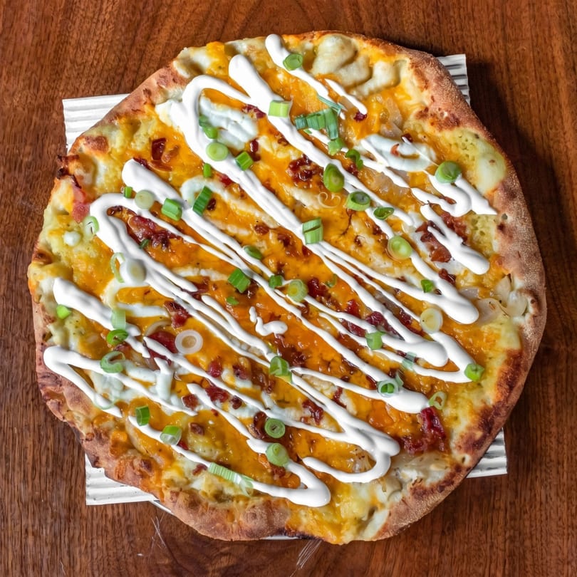Overhead view of a loaded baked potato pizza with cheese, bacon, sour cream, and green onions.